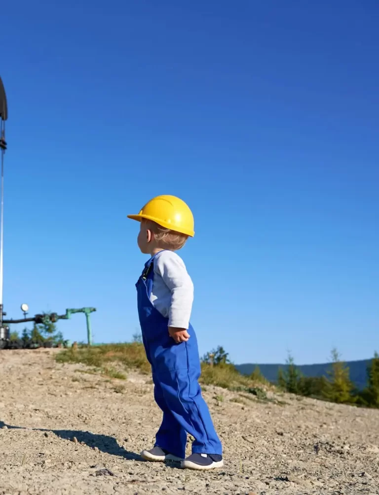 Child with helmet on backdrop of working oil borehole.